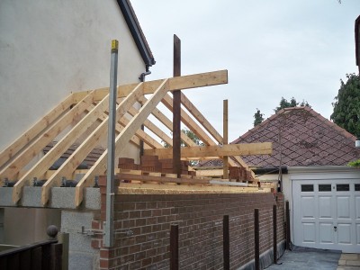 Installation of new roof trusses to form front porch and new extension roof. The roof extends to existing garage with a fibreglass flat roof in between.